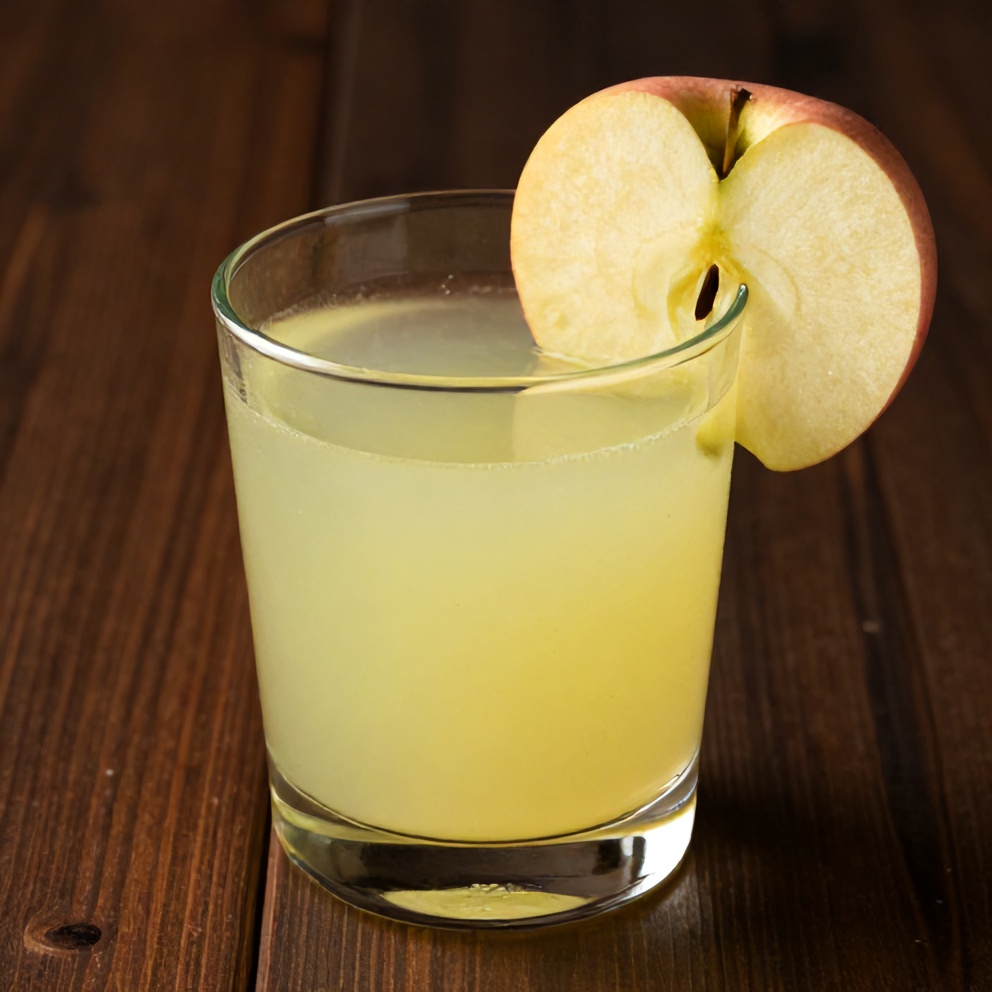 Glass of celery apple juice with a slice of apple on the rim